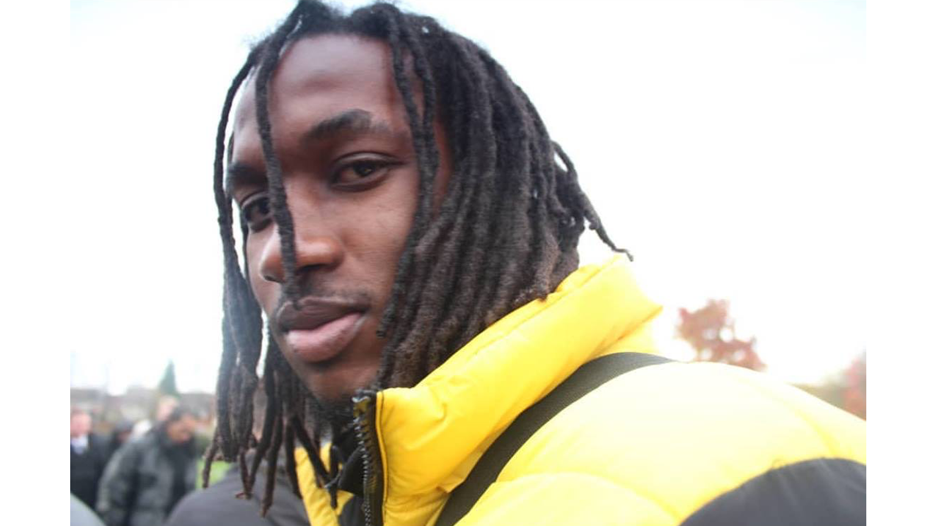 A man in dreadlocks and a yellow puffy jacket looks sideways on